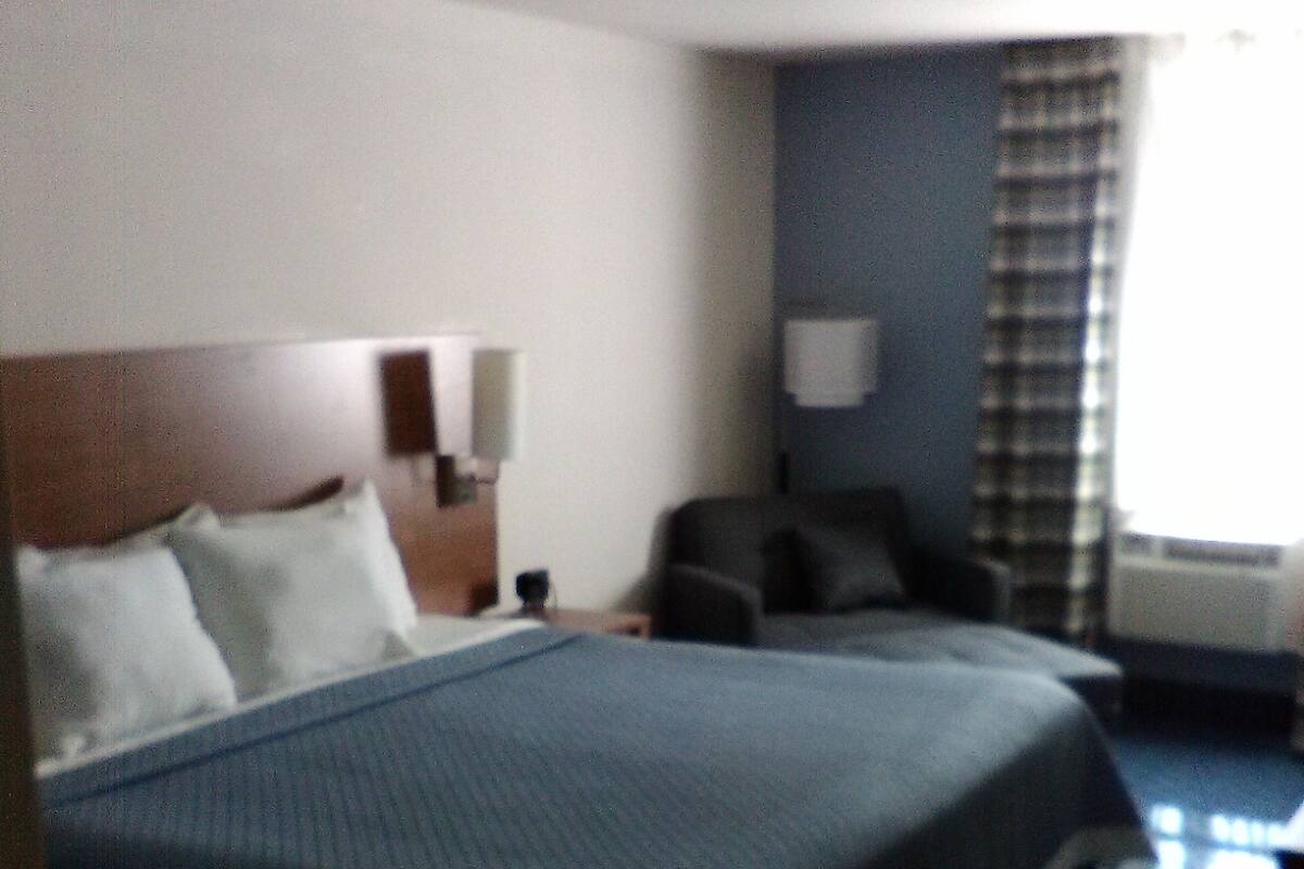 Una habitación de hotel con una cama grande, un escritorio, una silla y un ventanal con cortinas.