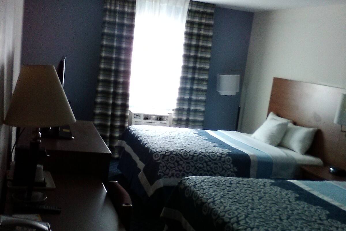 Una habitación de hotel con dos camas, un escritorio con lámpara y una ventana con cortinas.
