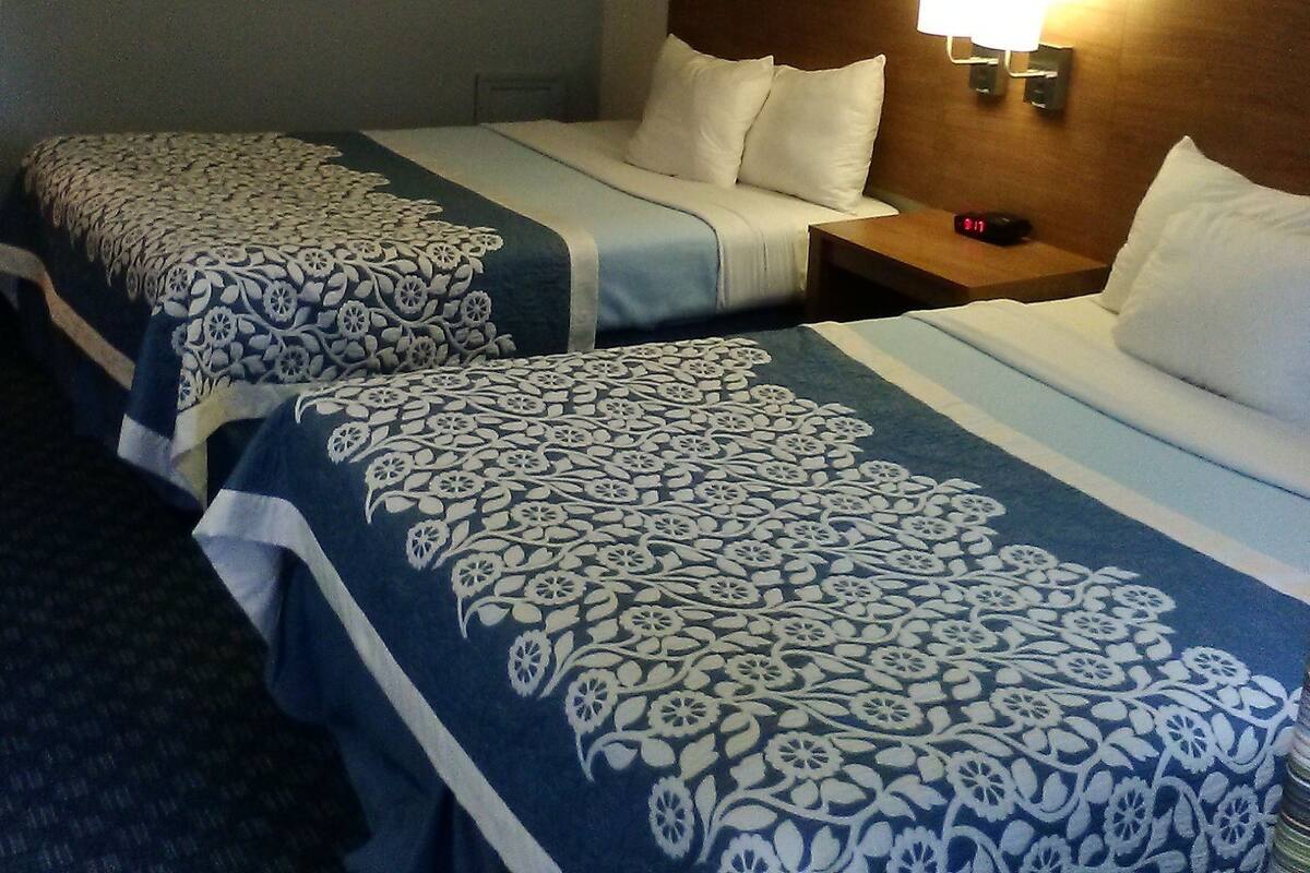Habitación de hotel con dos camas, cada una con ropa de cama estampada, una mesita de noche con lámpara y un espejo montado en la pared.