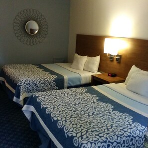 A hotel room with two beds, each with patterned bedding, a bedside table with a lamp, and a wall-mounted mirror.