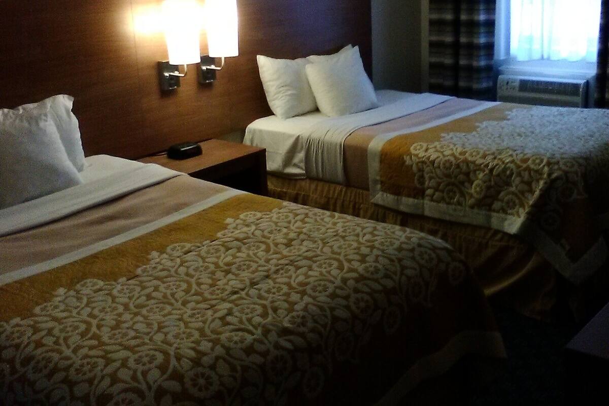 Una habitación de hotel con dos camas, una mesita de noche y una lámpara de pared.