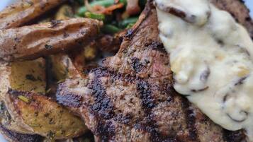 Une assiette de nourriture comprenant de la viande grillée, des pommes de terre rôties, des haricots verts et une sauce crémeuse.