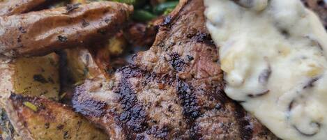 Un plato de comida con carne a la parrilla, papas asadas, judías verdes y salsa cremosa.