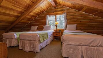 A cozy attic bedroom with two beds, a window, and a nightstand with a lamp.