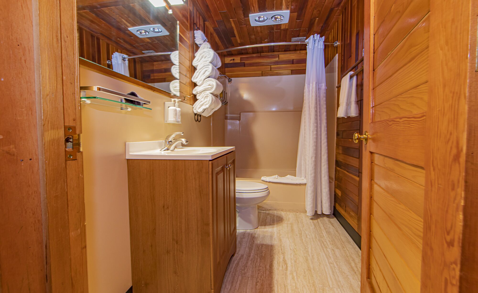 Un baño de madera con lavamanos, inodoro y cortina de ducha.