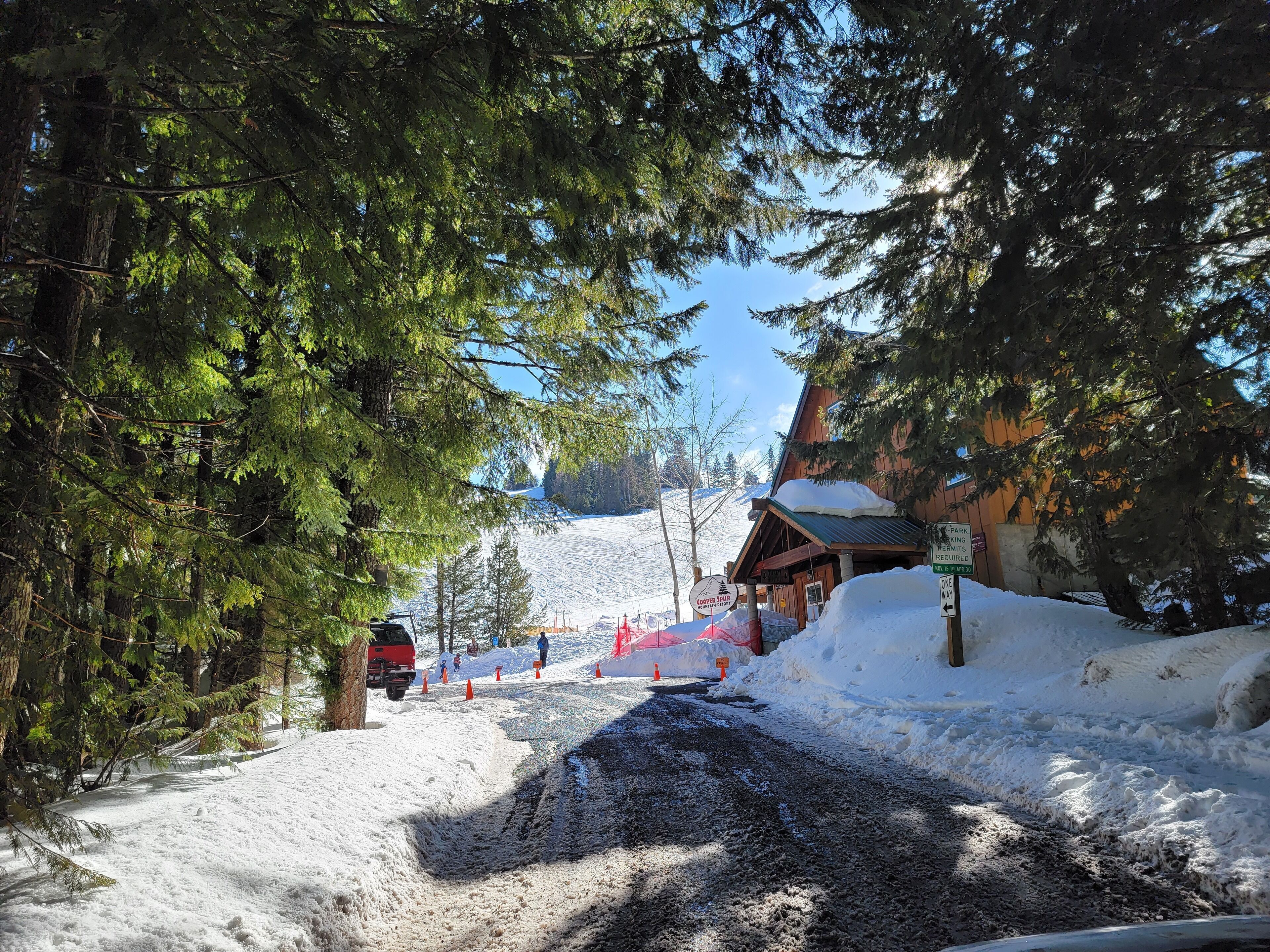 Camino cubierto de nieve que conduce a una cabaña con fachada de madera y un cartel que indica las normas de aparcamiento.