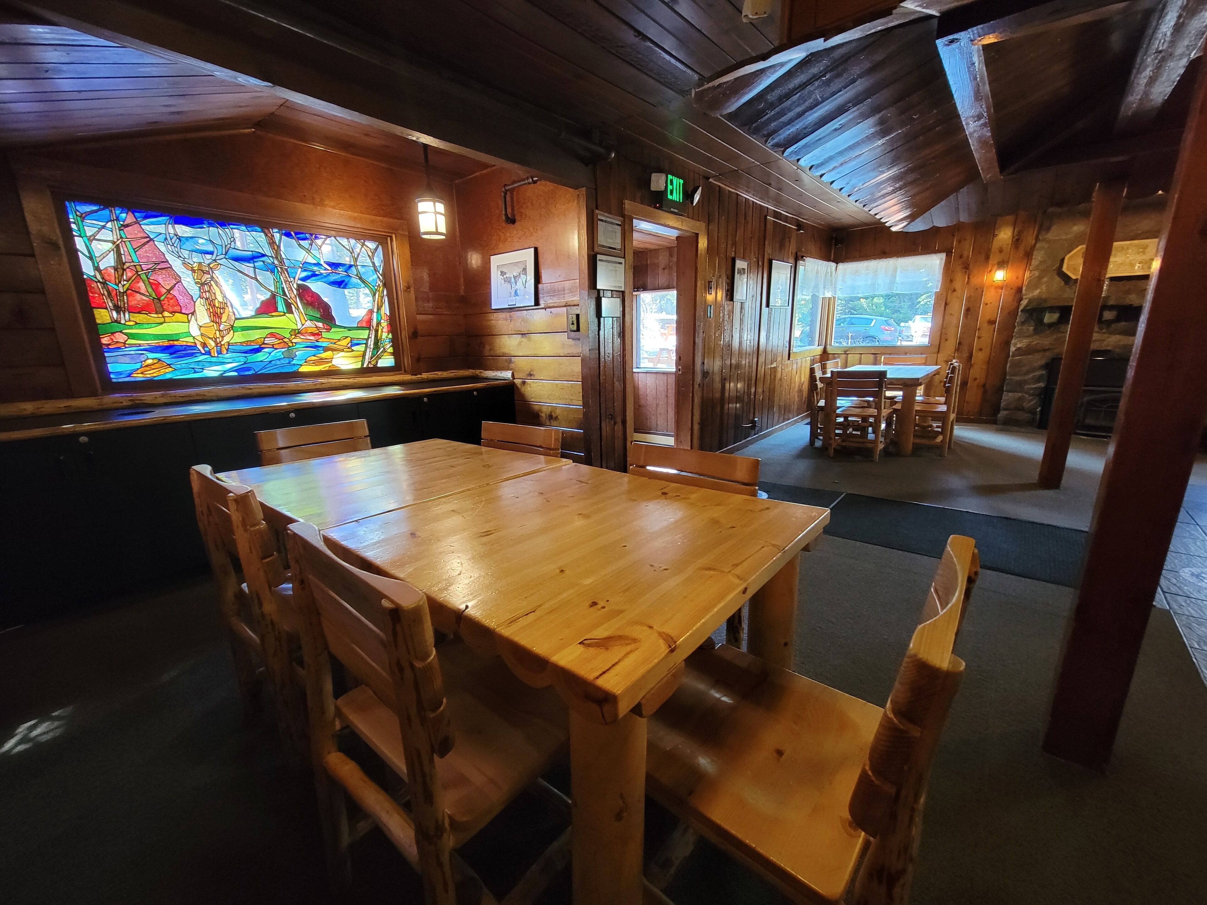 Un intérieur en bois agrémenté d’un vitrail, de tables et de chaises en bois, et offrant une vue sur l’extérieur.