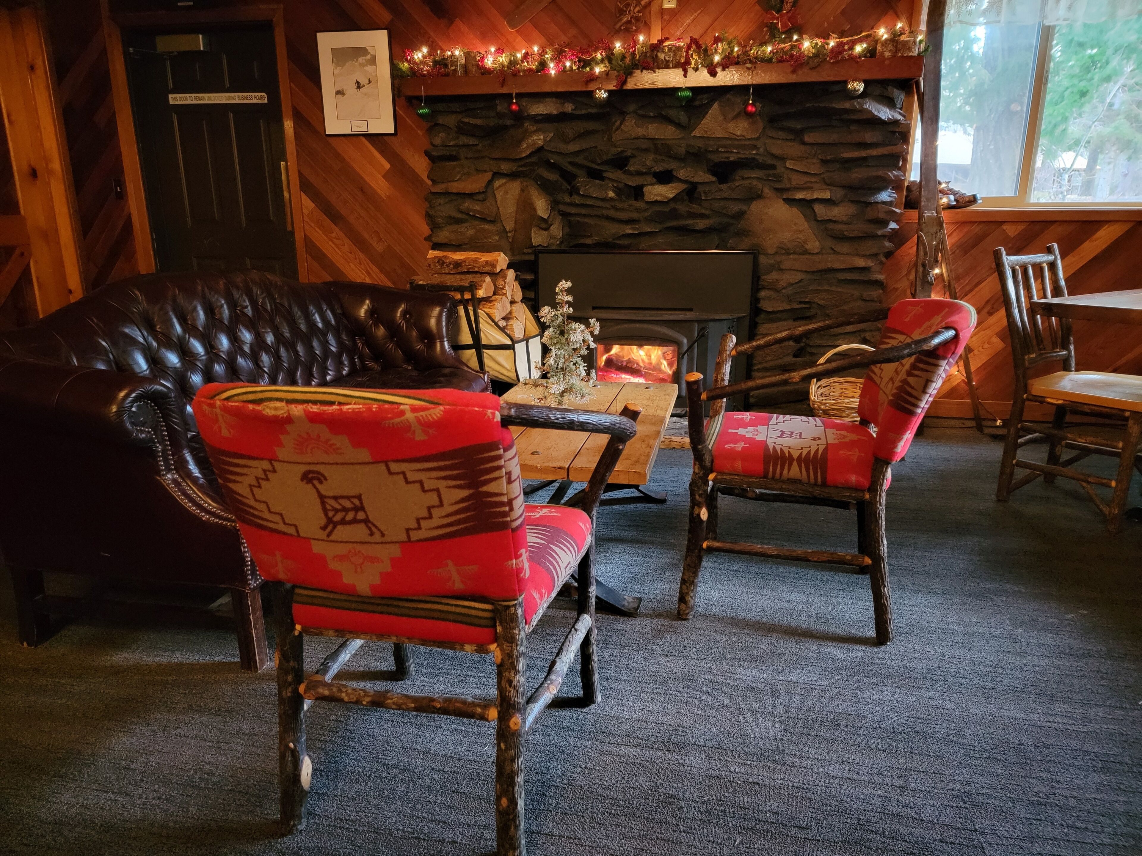 A cozy room with a stone fireplace, leather sofa, and rustic wooden chairs.