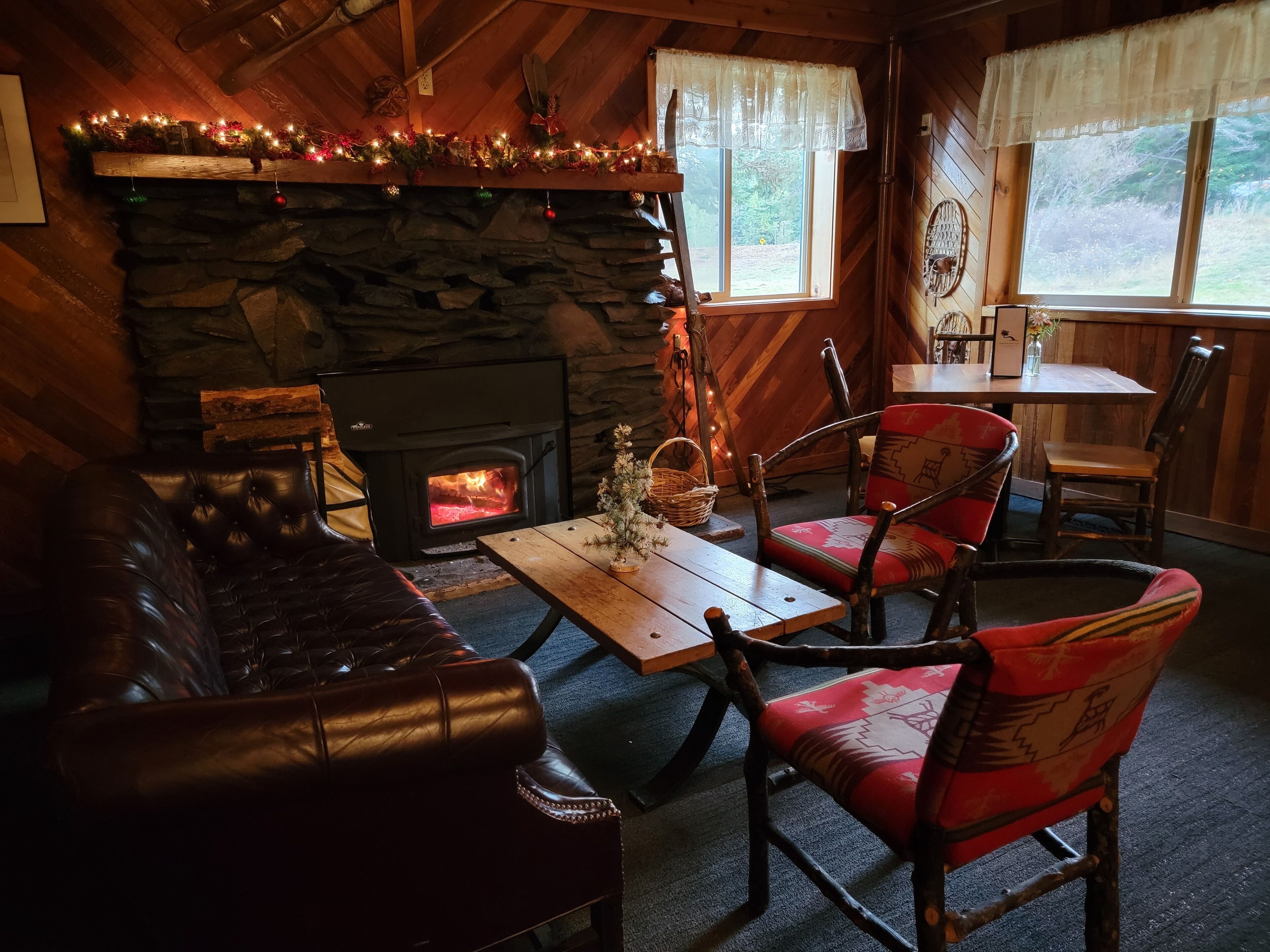Interior acolhedor de uma cabana com lareira de pedra, sofá de couro e mesa de jantar de madeira.