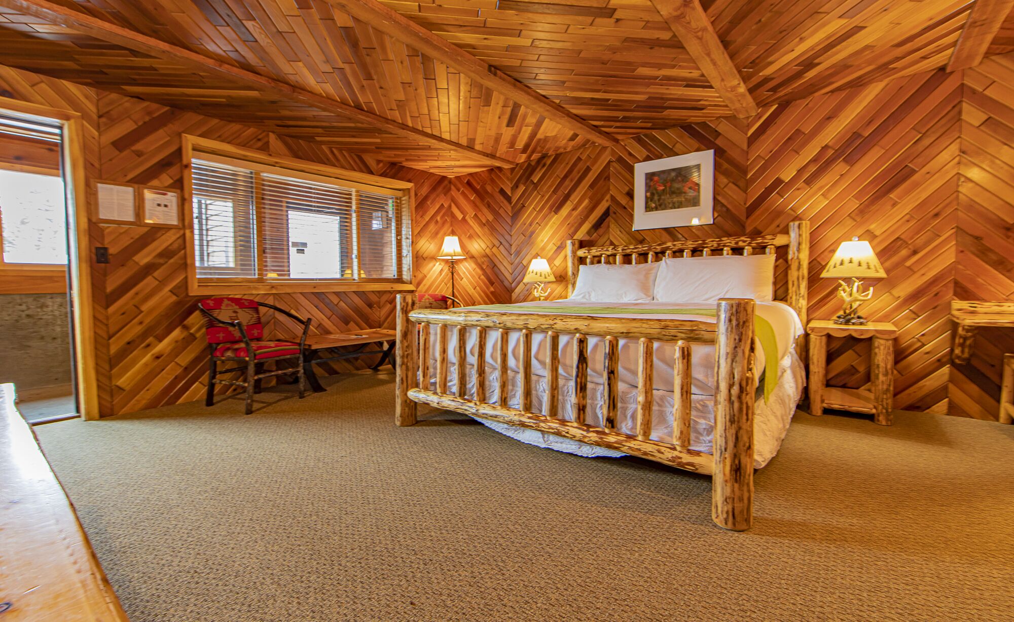 Una habitación con paneles de madera, una cama, dos lámparas de noche, un sillón y una ventana con persianas.