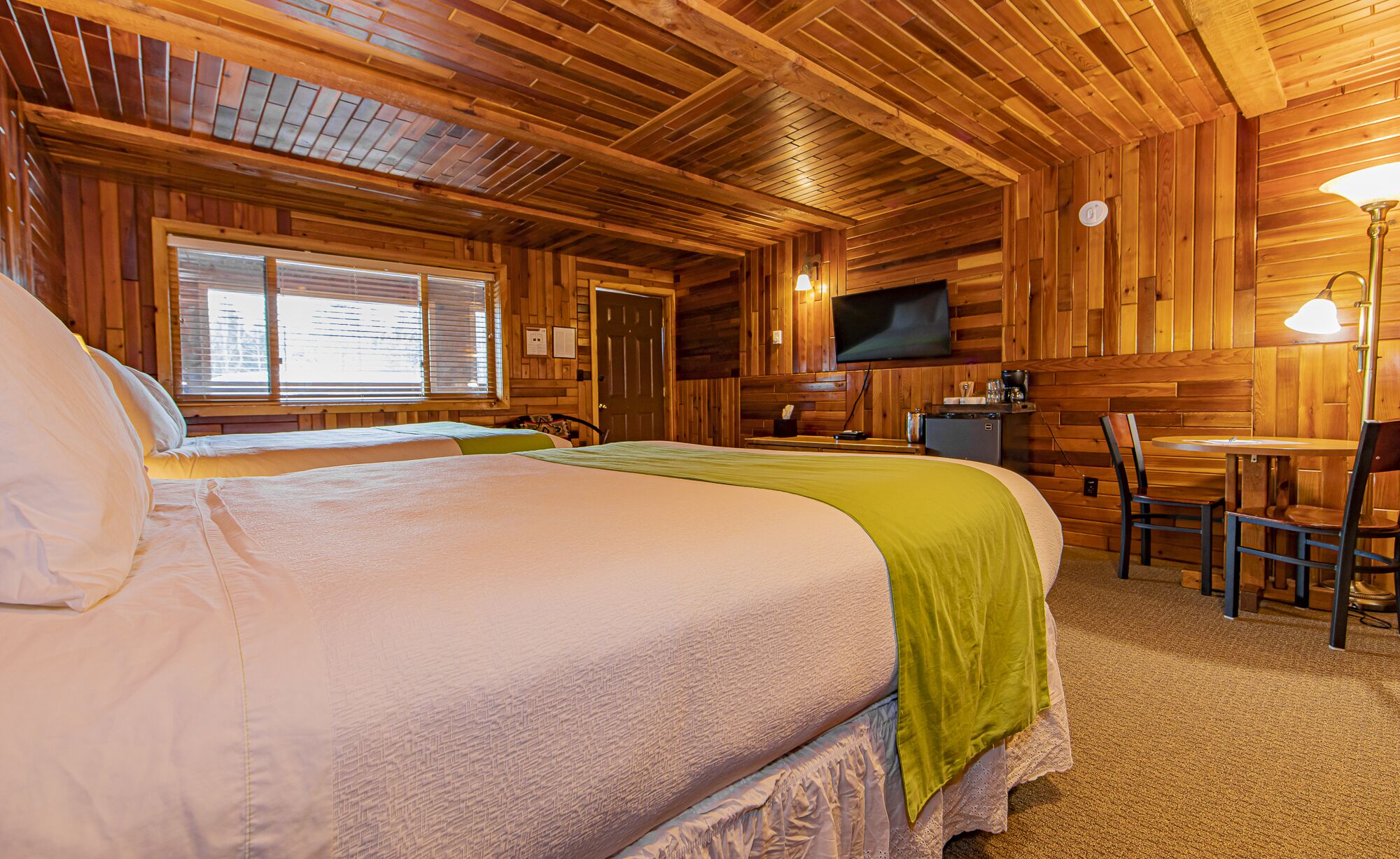 Une chambre dans un chalet en bois, équipée de deux lits, d’une télévision, d’un bureau et d’une chaise.