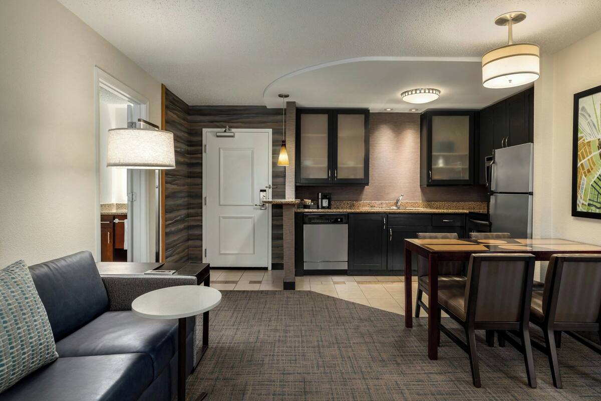 A modern kitchen with dark cabinets, a refrigerator, and a dining area with a table and chairs.