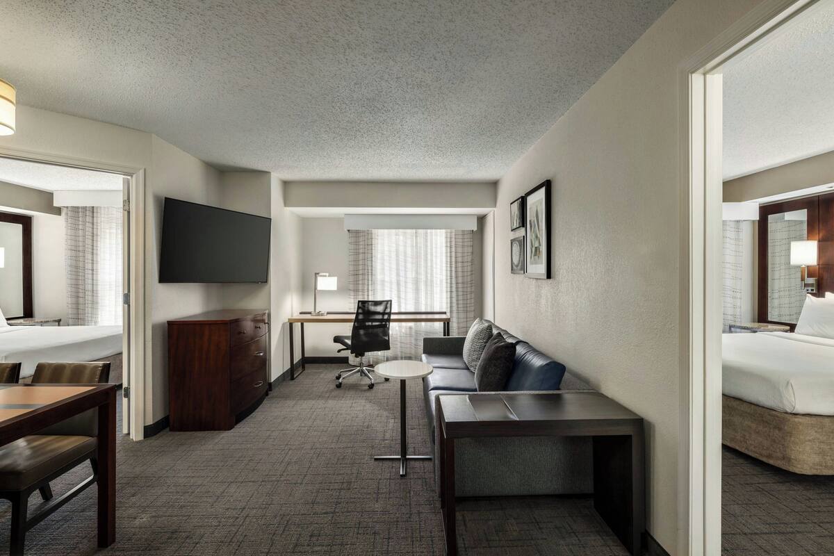 A hotel room with a bed, a desk, a chair, a sofa, and a TV.