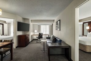 A hotel room with a bed, a desk, a chair, a sofa, and a TV.