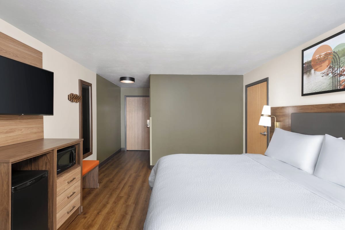A hotel room with a bed, a TV, a desk with a microwave, and a door leading to another room.