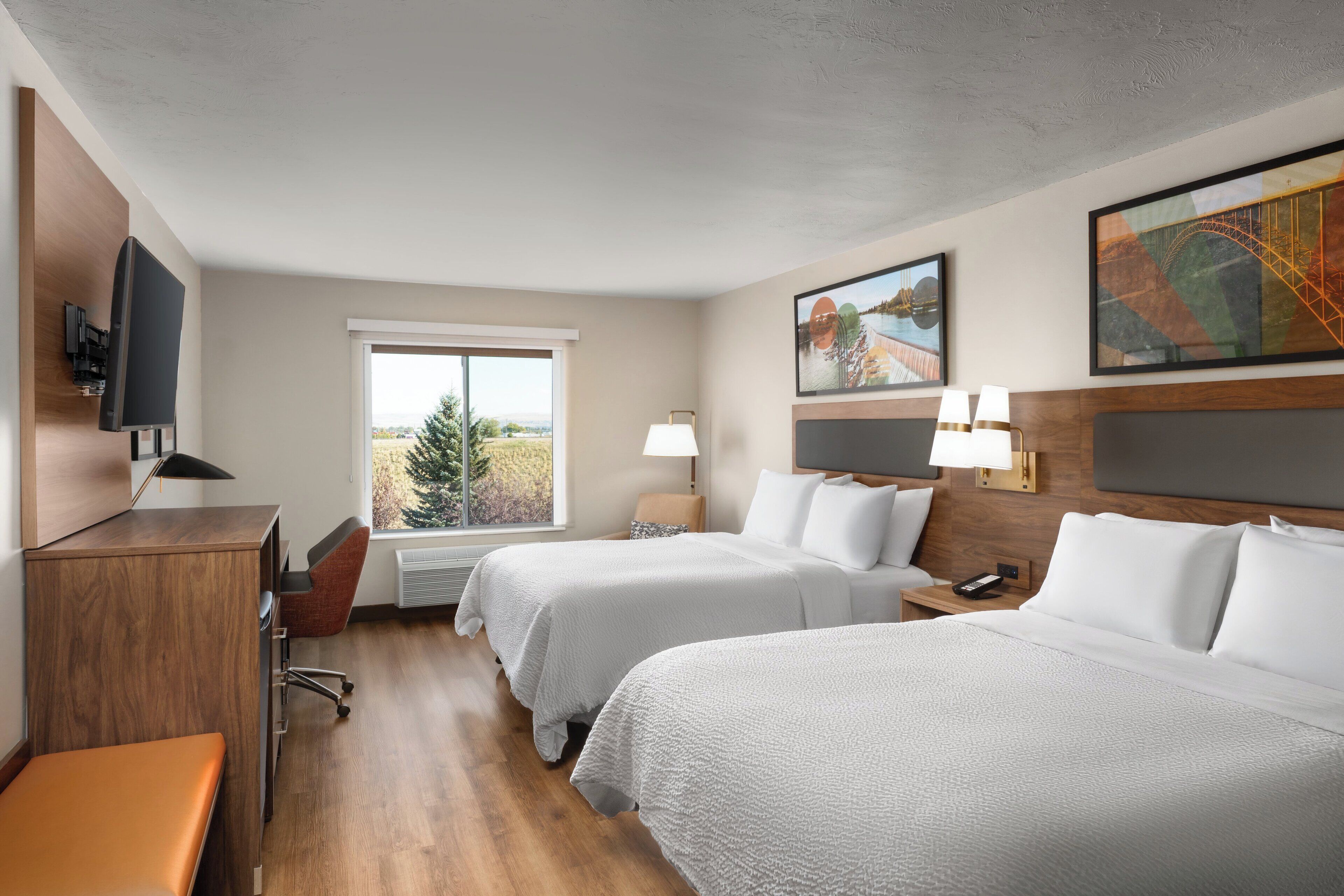 A hotel room with two beds, a desk, a chair, a TV, and a window with a view.