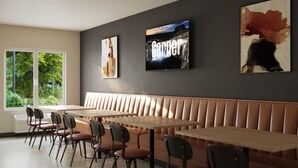 A modern dining area with a long wooden table, cushioned benches, and a large window offering a view of greenery.