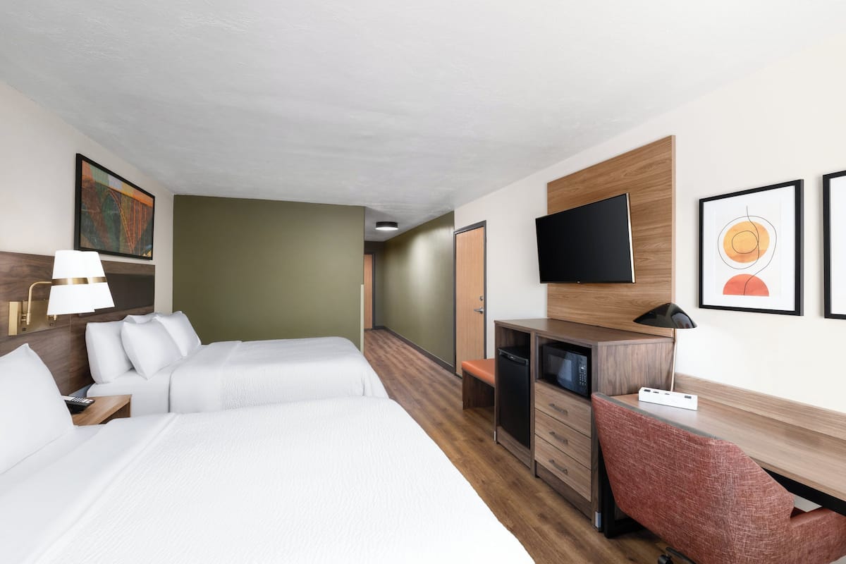 A hotel room with two beds, a desk, a television, and artwork on the walls.