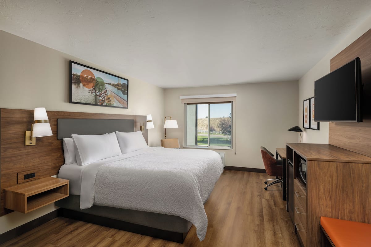 Ein modernes Hotelzimmer mit einem großen Bett, Nachttischen, einem Schreibtisch und einem Fernseher.