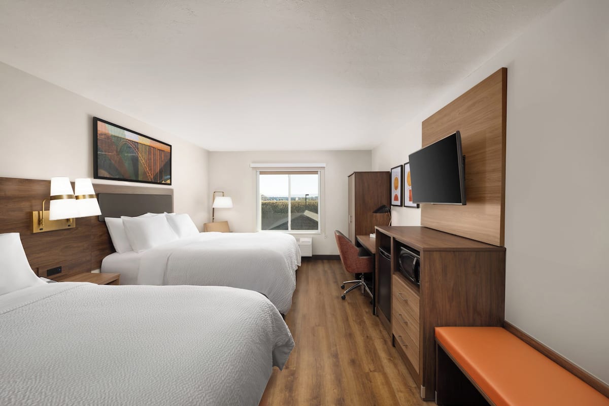 A hotel room with two beds, a desk, a chair, a television, and a window with a view.