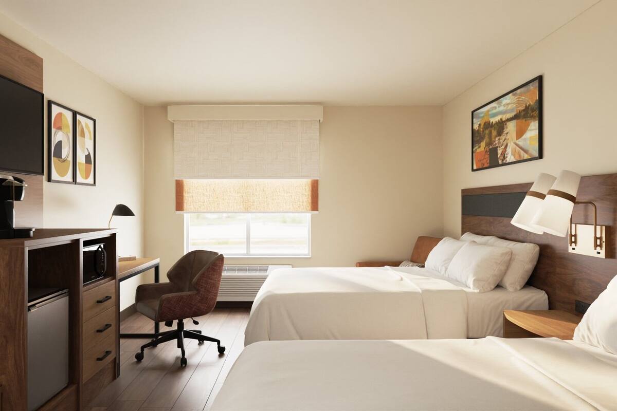 Ein Hotelzimmer mit zwei Betten, einem Schreibtisch, einem Stuhl, einem Fernseher und einem Fenster mit Jalousien.