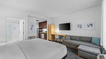 A hotel room with a bed, a sofa, a desk, a chair, and a TV.