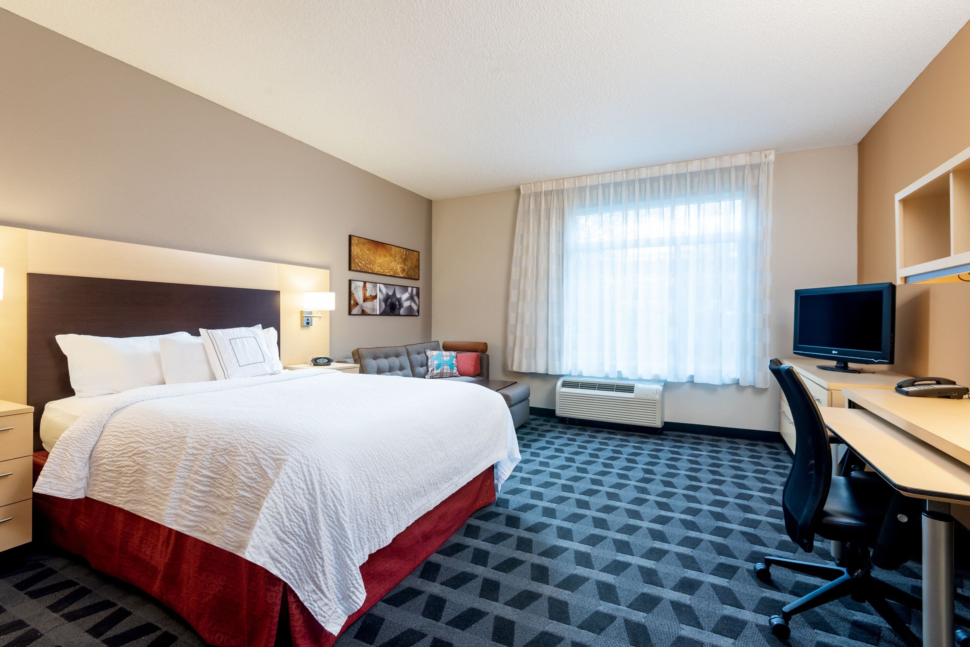 Una habitación de hotel con una cama grande, un escritorio, una silla, un televisor y una ventana con cortinas.
