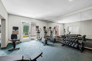 Un gimnasio con máquinas de cardio, mancuernas y un espejo grande.