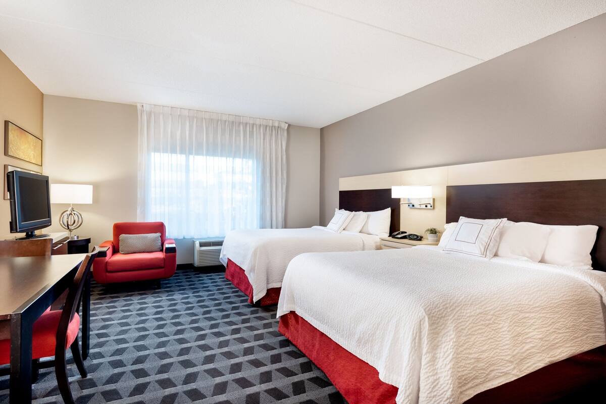 Hotelkamer met twee bedden, een bureau, een stoel, een televisie en een raam met gordijnen.