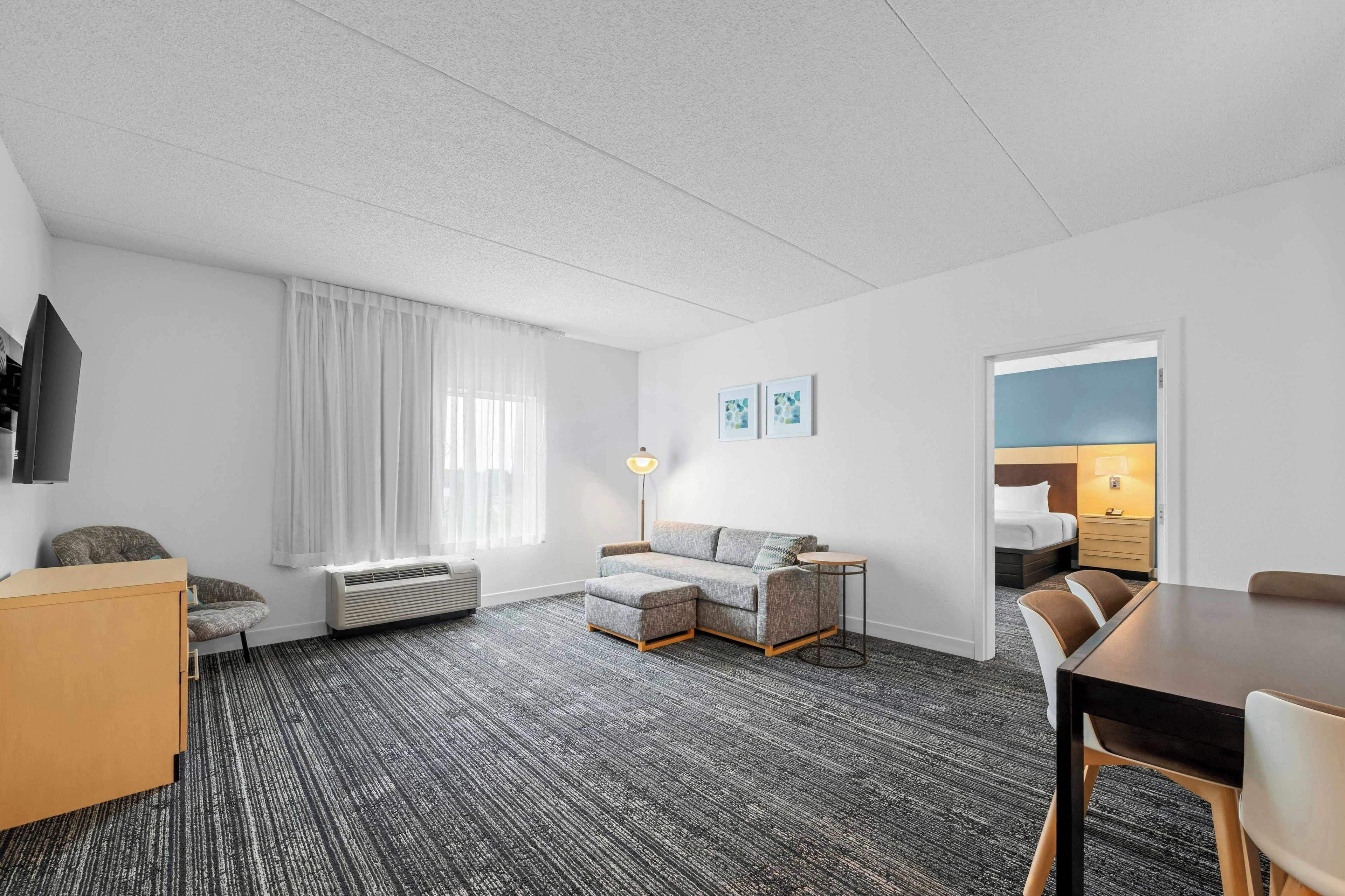Habitación de hotel con sofá, una mesita, una silla, televisión, lámpara y cama.