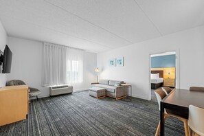 A hotel room with a sofa, a small table, a chair, a TV, a lamp, and a bed. - TownePlace Suites by Marriott Mooresville (Mooresville)