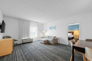 Habitación de hotel con sofá, una mesita, una silla, televisión, lámpara y cama.