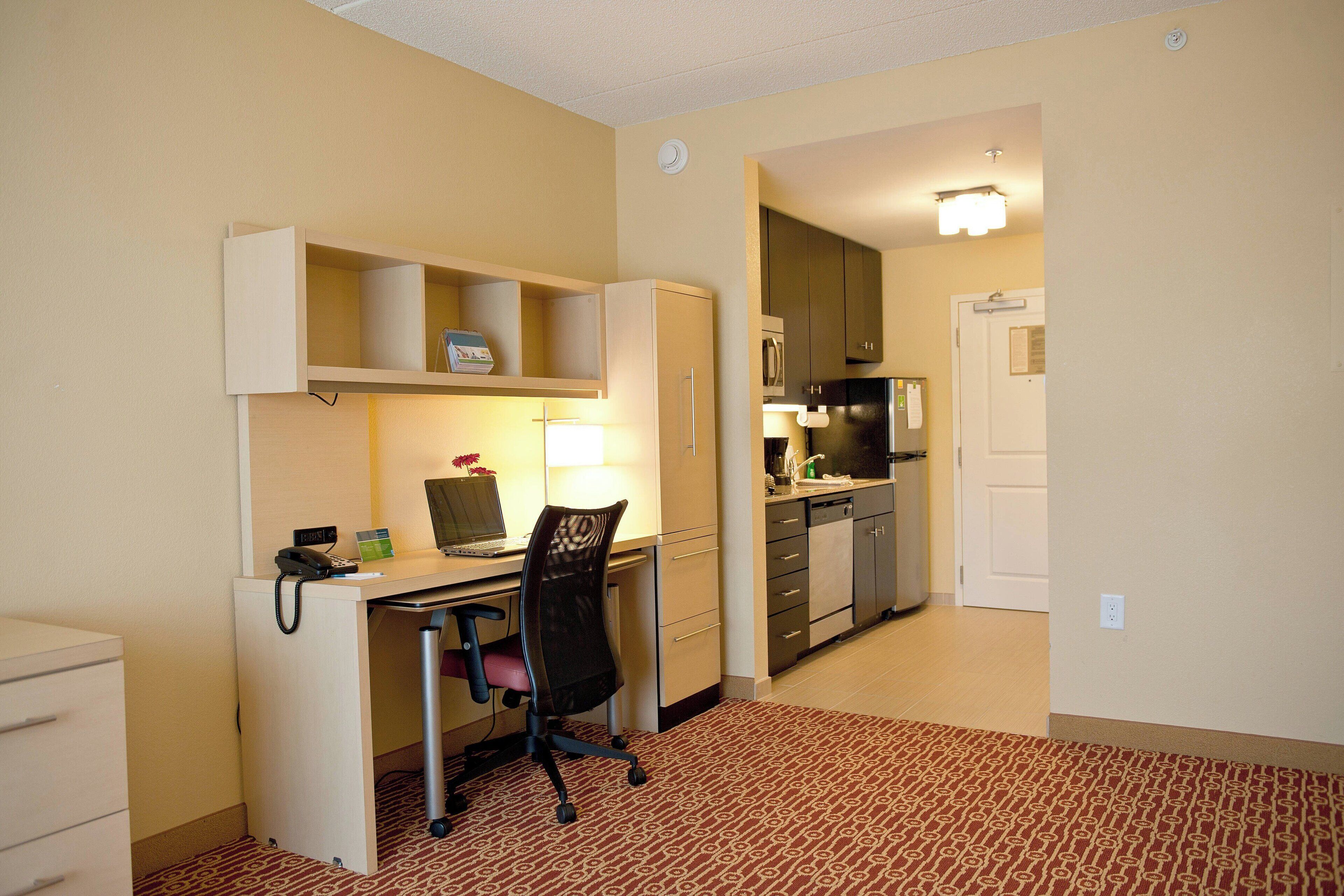 Habitación de hotel con escritorio, silla y kitchenette.