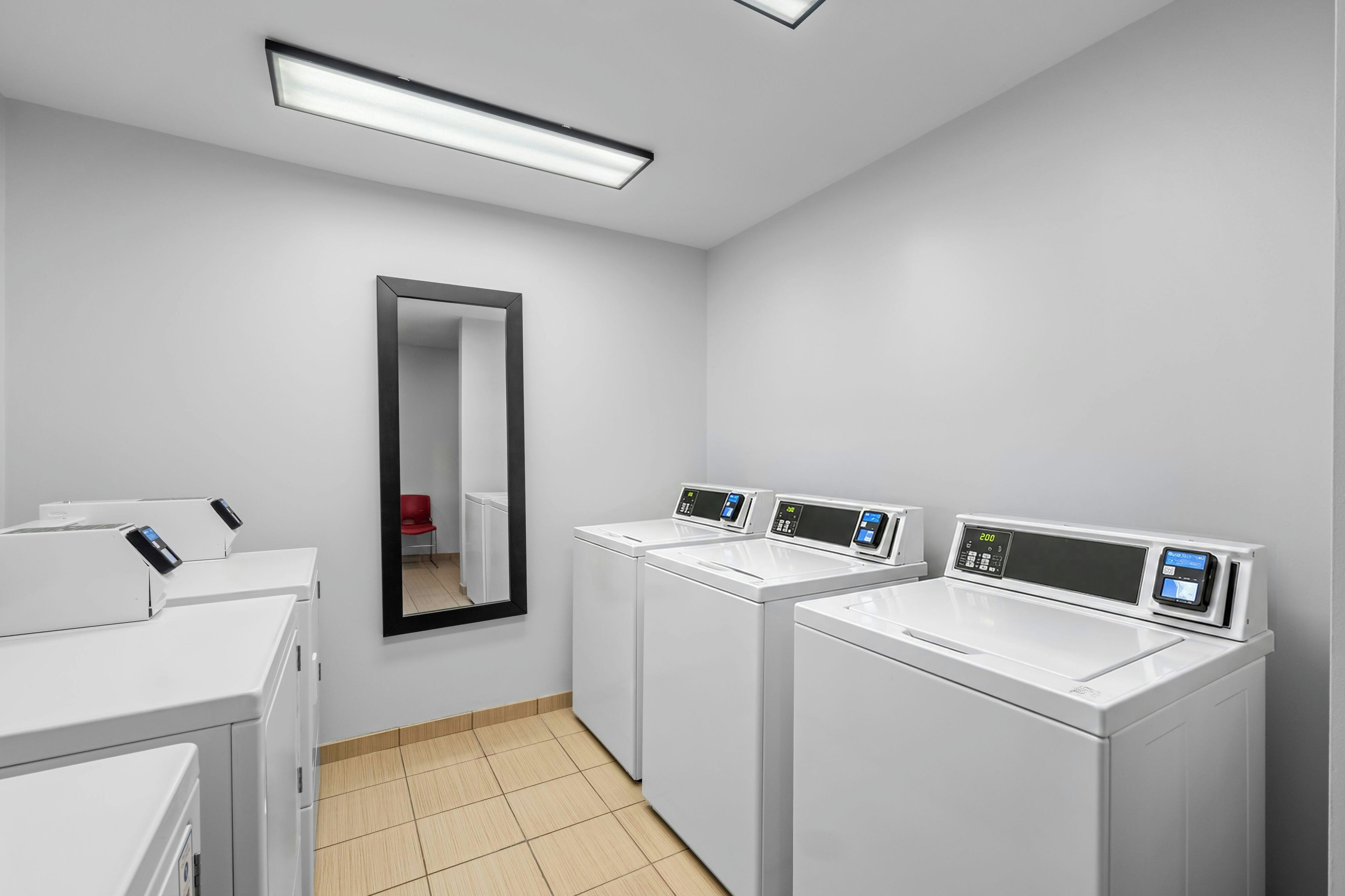 A laundry room with white appliances, a mirror, and a tiled floor.