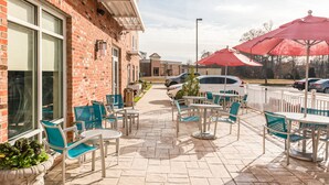 Un patio al aire libre con paredes de ladrillo, mobiliario exterior y sombrillas rojas.