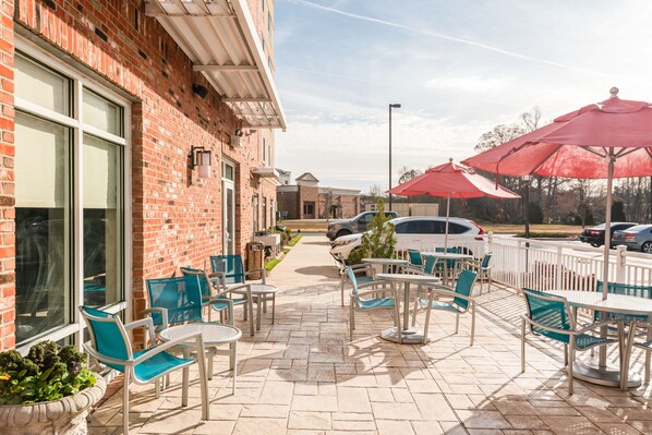 Een terras buiten met bakstenen muren, zitplaatsen en rode parasols.