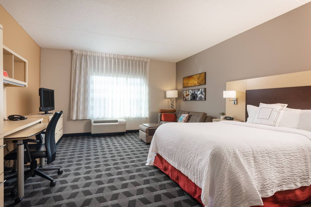 Een hotelkamer met een bed, bureau, stoel en een raam met gordijnen.