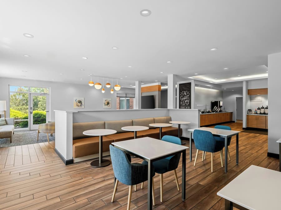 A modern interior with a seating area, tables, a kitchen, and a view of greenery.