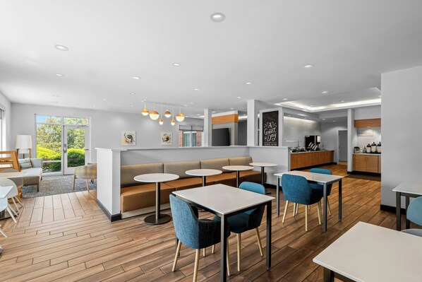 Un interior moderno con zona de estar, mesas, cocina y vistas a zonas verdes.