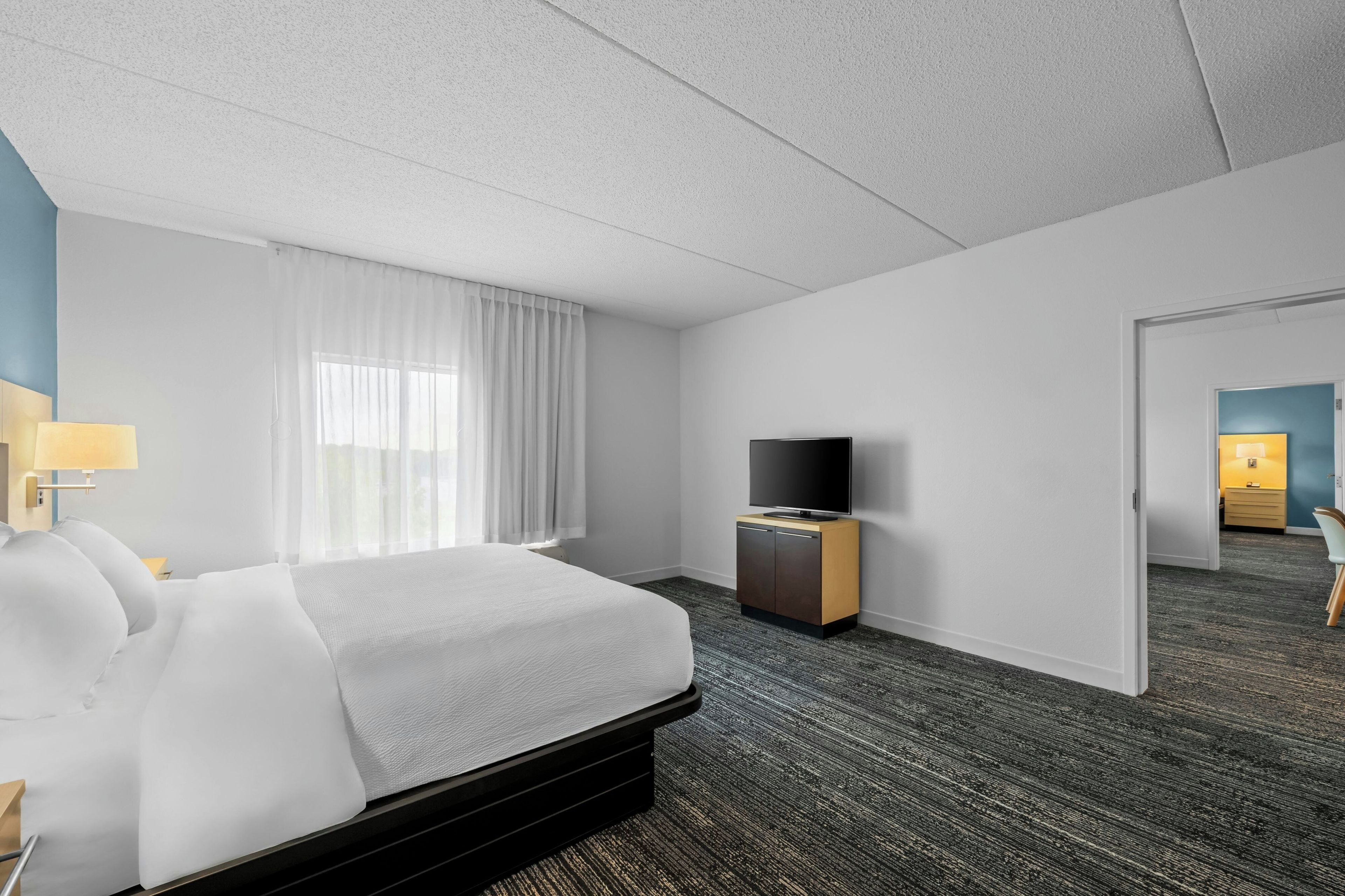 A hotel room with a bed, a television on a wooden cabinet, and a door leading to another room.