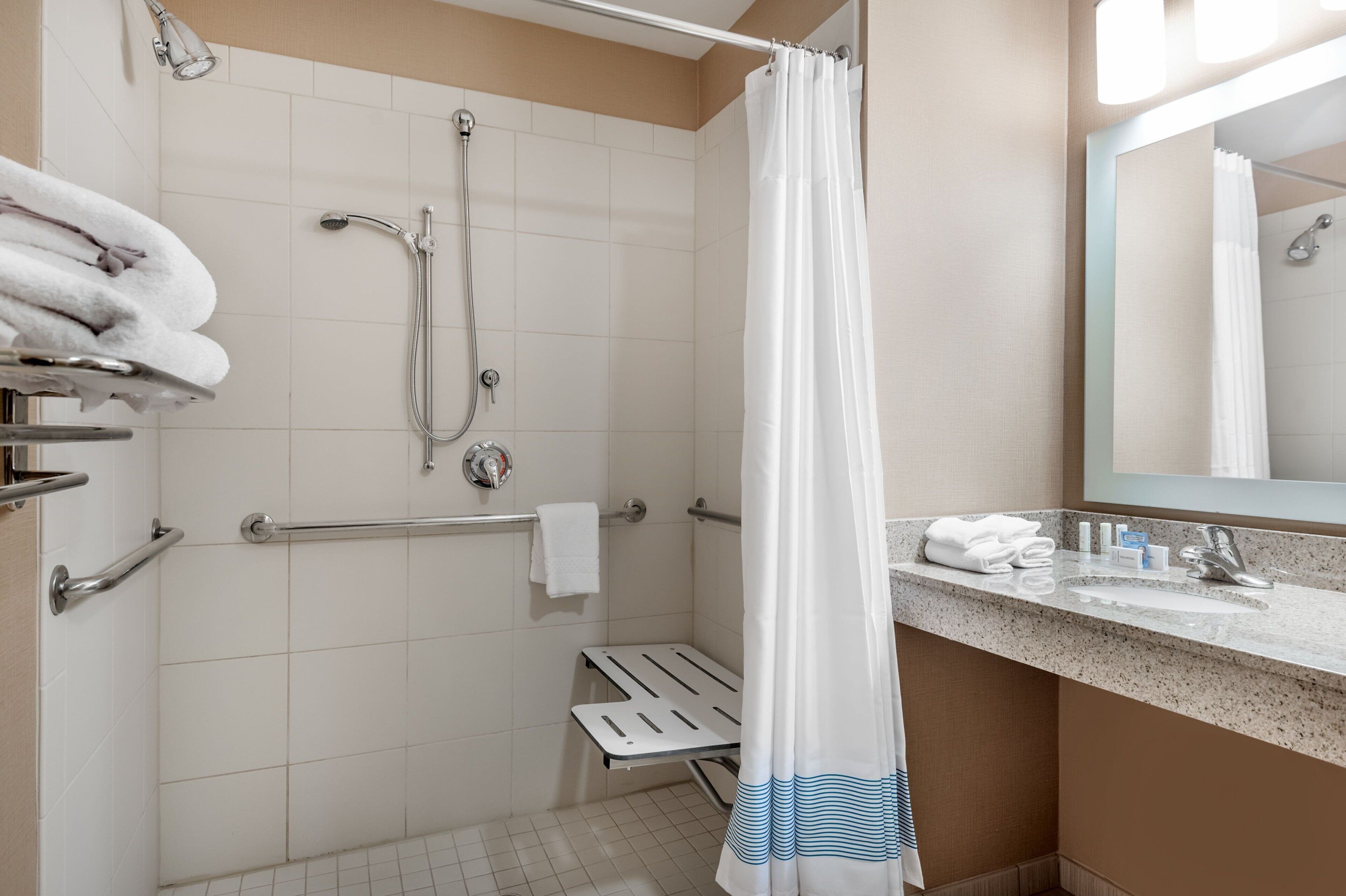 Un baño con ducha, barras de apoyo, toallero y lavamanos con artículos de aseo.