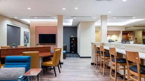 Un moderno vestíbulo de hotel con zona de comedor, bar y mostrador de recepción.