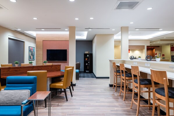 Un hall d’hôtel moderne comprenant un espace repas, un bar et un comptoir d’accueil.
