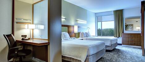 A hotel room with two beds, a desk with a chair, a mirror, and a window with curtains.