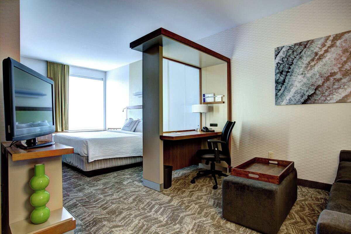 Ein Hotelzimmer mit Bett, Schreibtisch, Stuhl, Fernseher und einem Bild an der Wand.