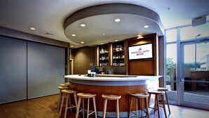 Un espace bar avec des tabourets en bois, un comptoir et un grand écran affichant le nom de l’hôtel.