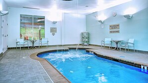 Une piscine intérieure avec un sol carrelé, un escalier pour accéder à la piscine et un panneau indiquant qu’il n’y a pas de sauveteur en service.