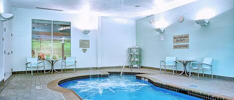 Una piscina interior con suelo de baldosas, una escalera de piscina y un cartel que indica que no hay socorrista de servicio.