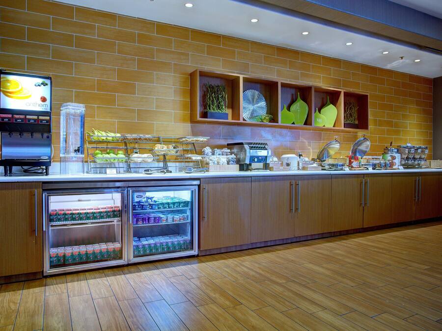 A breakfast bar with a beverage dispenser, a coffee machine, and a refrigerated display.