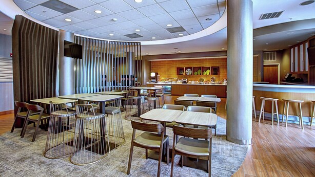 Un intérieur de restaurant moderne avec des tables rondes, des chaises, un bar et un mur en briques orné d’œuvres d’art.